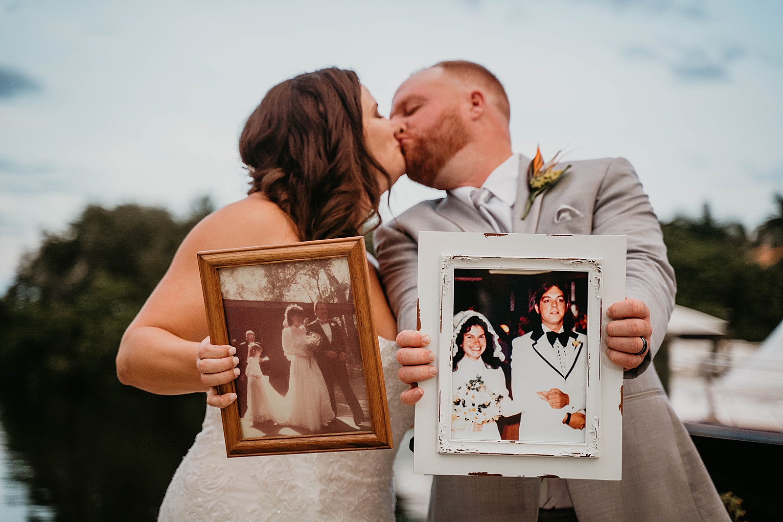 Bride and Groom kissing while holding vintage portraits of their parent's wedding Jupiter Lighthouse Wedding Photography captured by South Florida Wedding Photographer Krystal Capone Photography