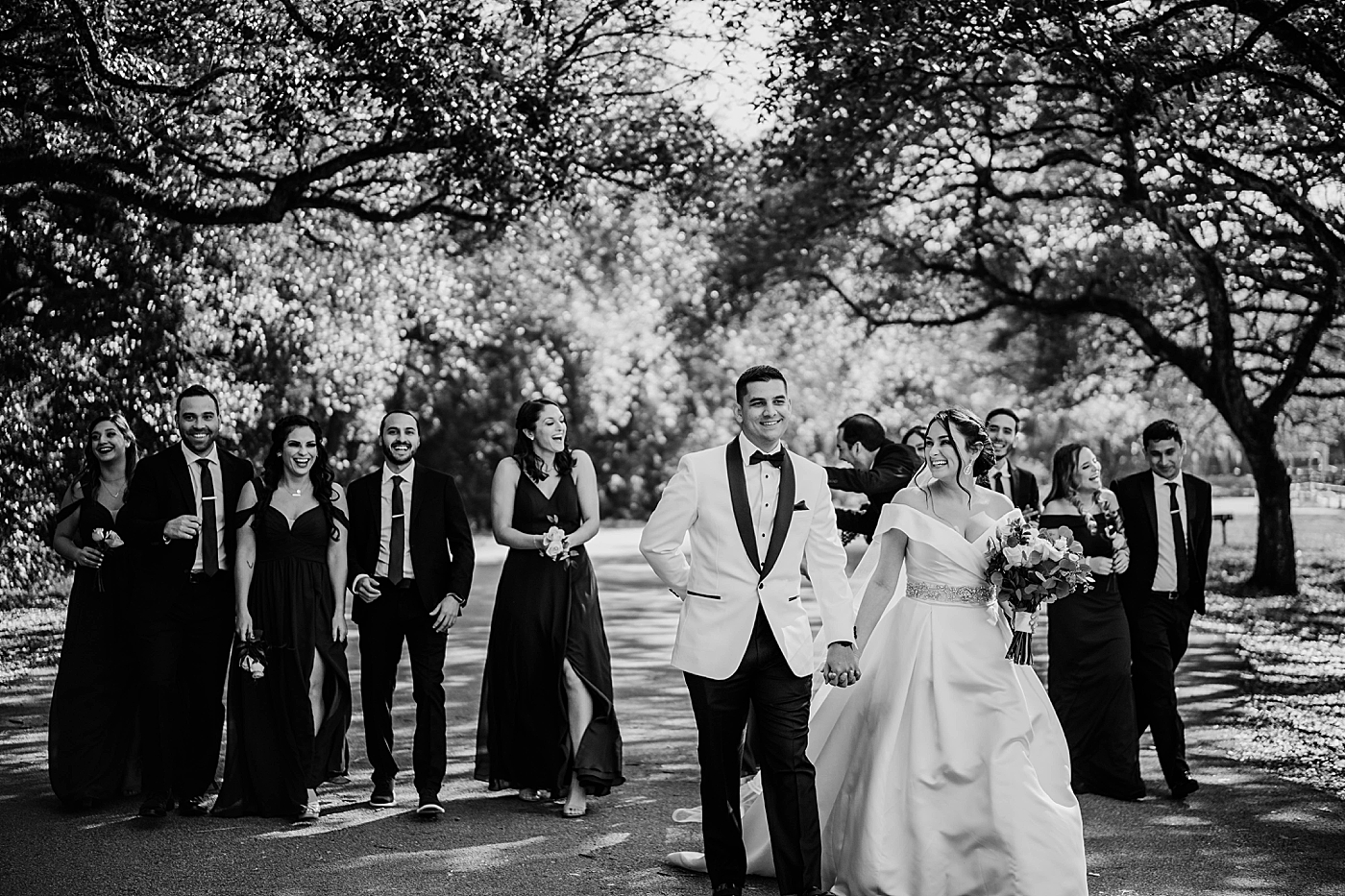 B&W Bride and Groom walking together with Wedding party following behind Lavan Venue Wedding Photography captured by South Florida Wedding Photographer Krystal Capone Photography