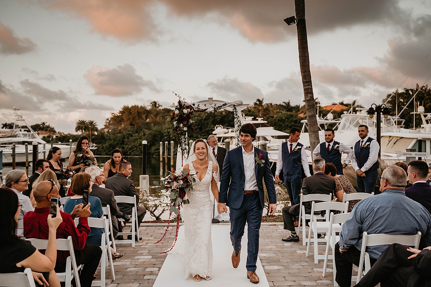 Bride and Groom exiting hand in hand with marina boats behind them Out of the Blue Celebrations Wedding Photography captured by South Florida Wedding Photographer Krystal Capone Photography 