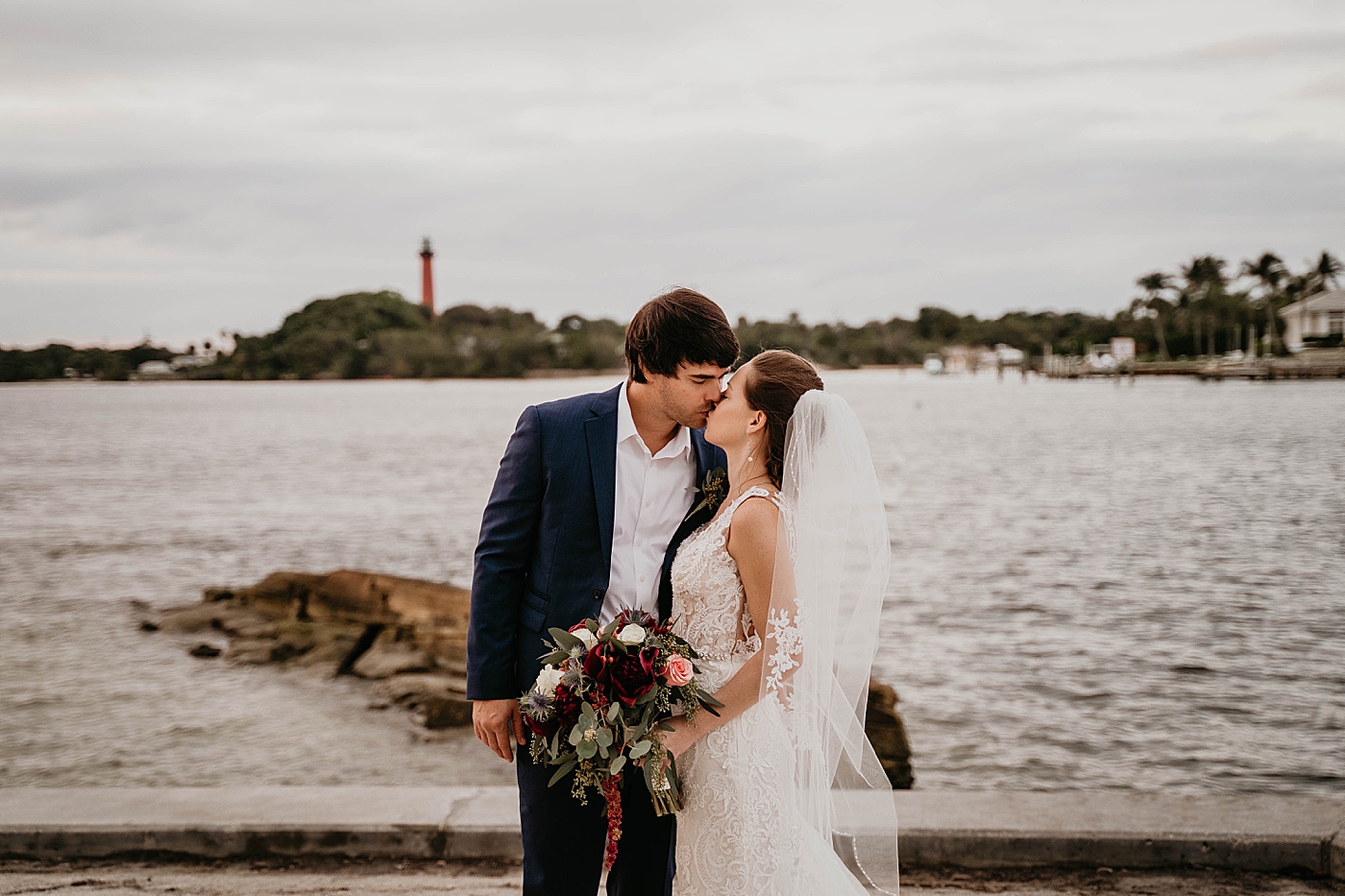 Bride and Groom kissing in front of ocean with lighthouse in the distance Out of the Blue Celebrations Wedding Photography captured by South Florida Wedding Photographer Krystal Capone Photography 