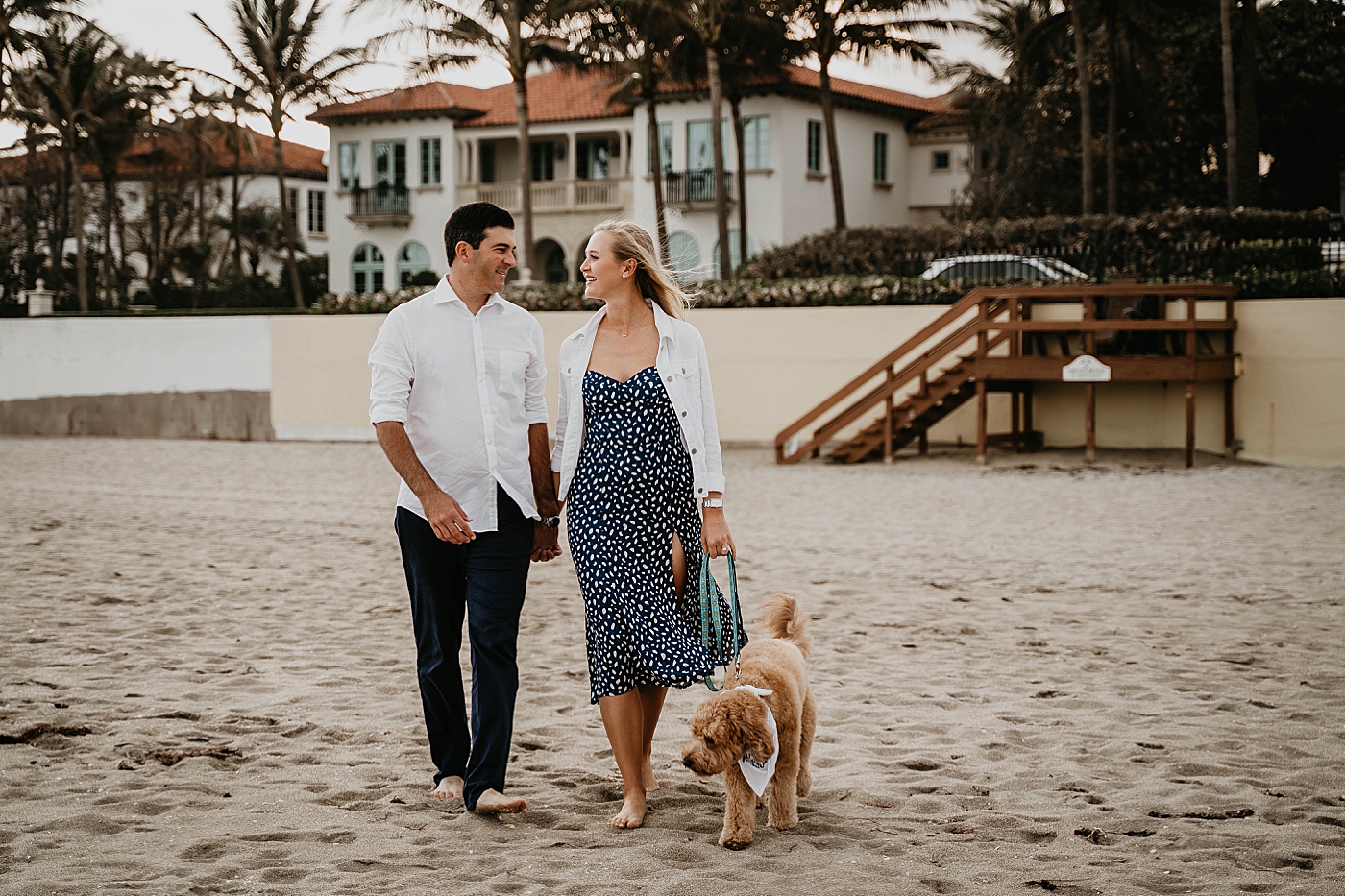 Couple walking dog on the beach with beach houses behind them Palm Beach Engagement Photography captured by South Florida Engagement Photographer Krystal Capone Photography 