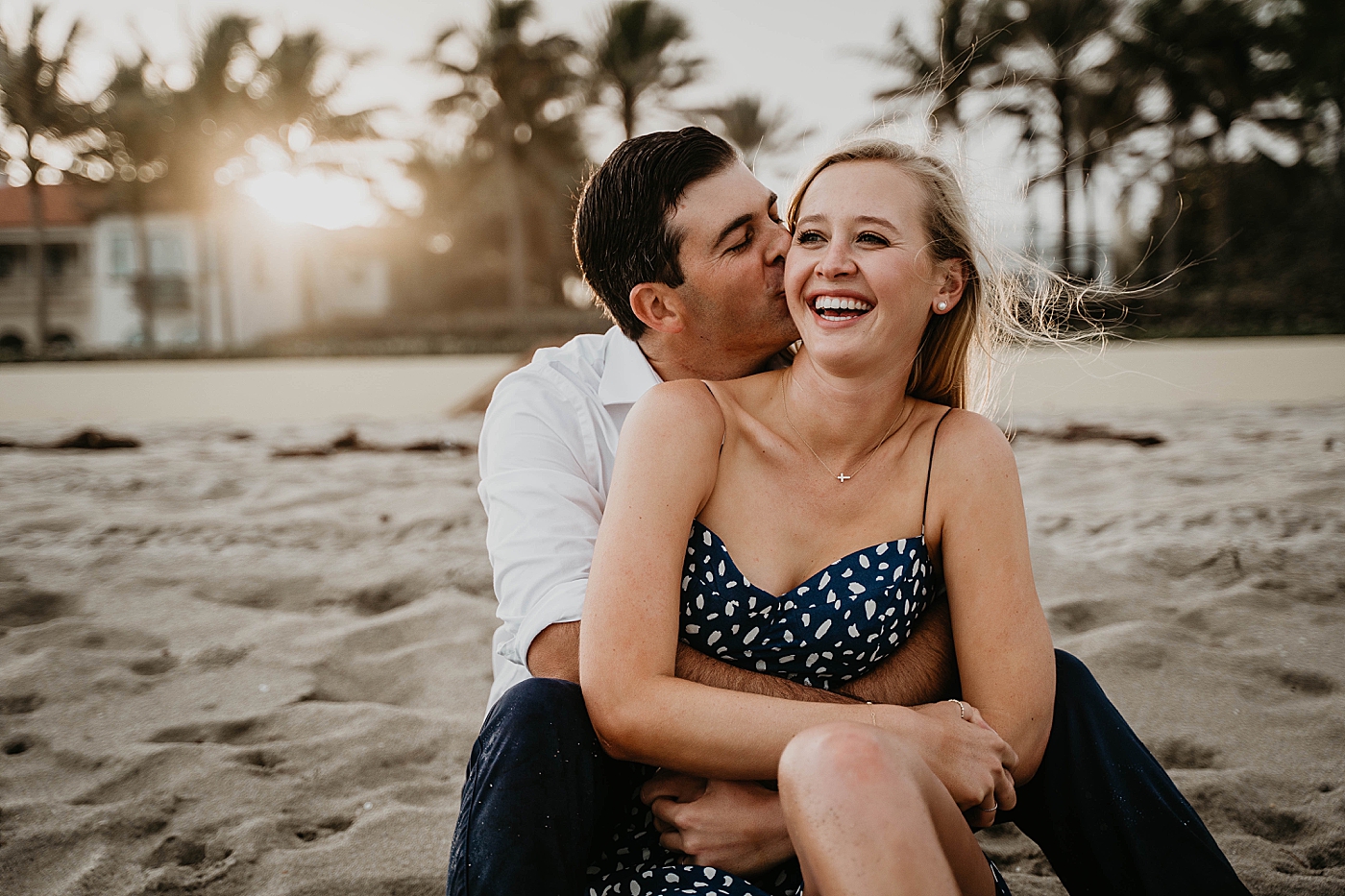 Couple sitting on the sand with man kissing woman on the cheek as sun sets Palm Beach Engagement Photography captured by South Florida Engagement Photographer Krystal Capone Photography 