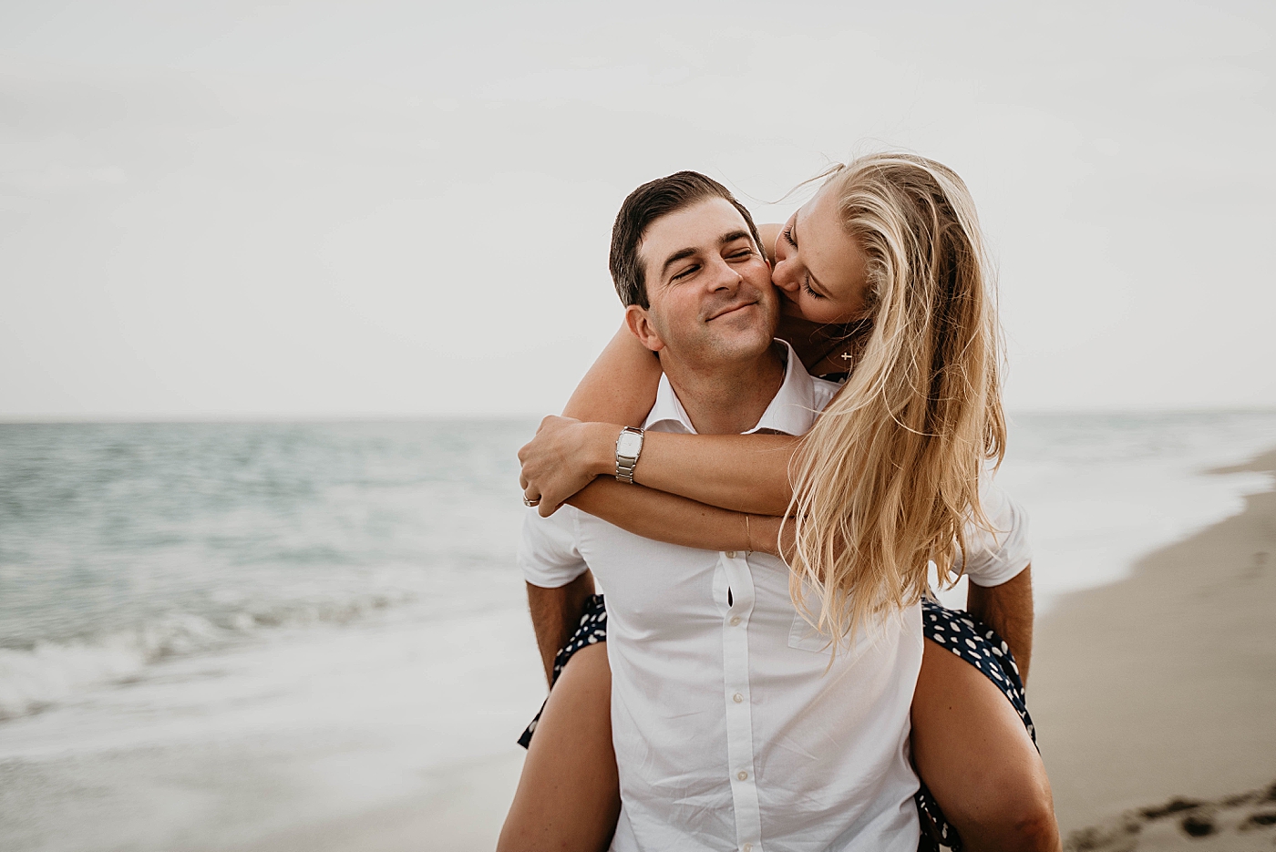 Couple piggy backing down the shoreline Palm Beach Engagement Photography captured by South Florida Engagement Photographer Krystal Capone Photography 
