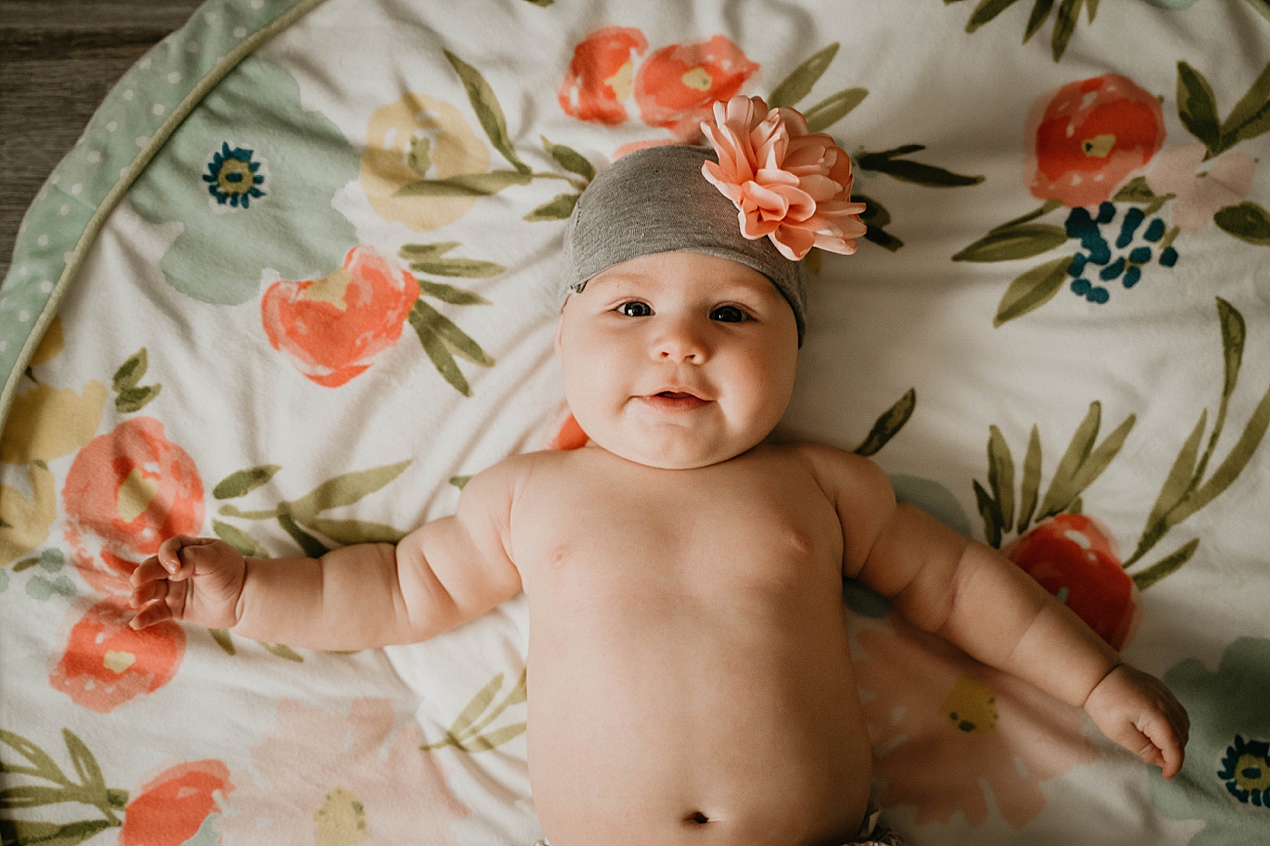 Baby laying down wearing gray hat with bright pink flower At Home South Florida Family Photography captured by South Florida Family Photographer Krystal Capone Photography 