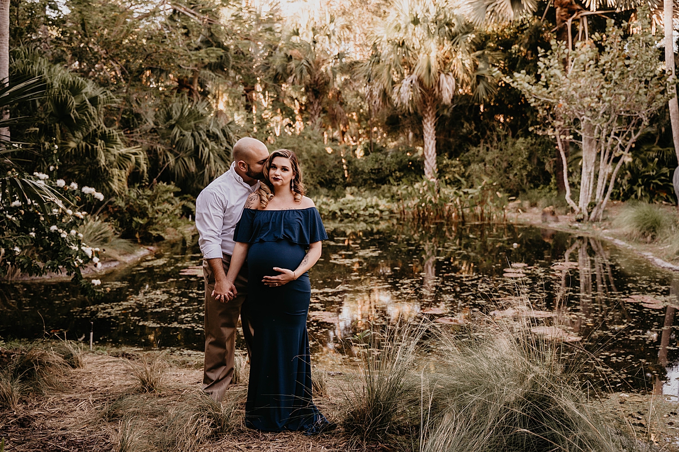 Husband holding wife's hand and kissing her by the lake South Florida Maternity Photography captured by South Florida Family Photographer Krystal Capone Photography 