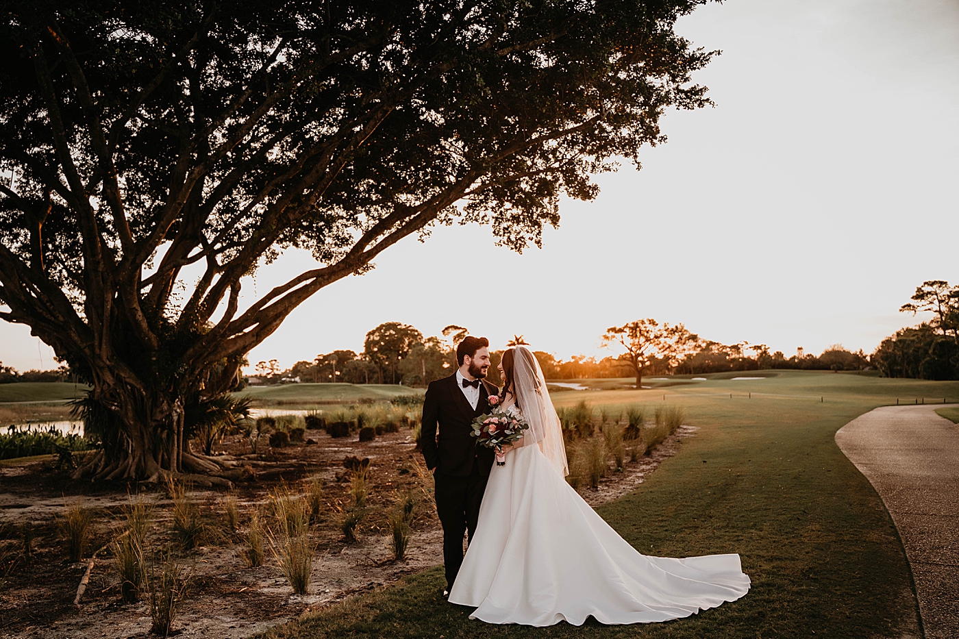 Bride and Groom looking at each other by a large tree as the sun sets Breakers West Wedding Photography captured by South Florida Wedding Photographer Krystal Capone Photography 