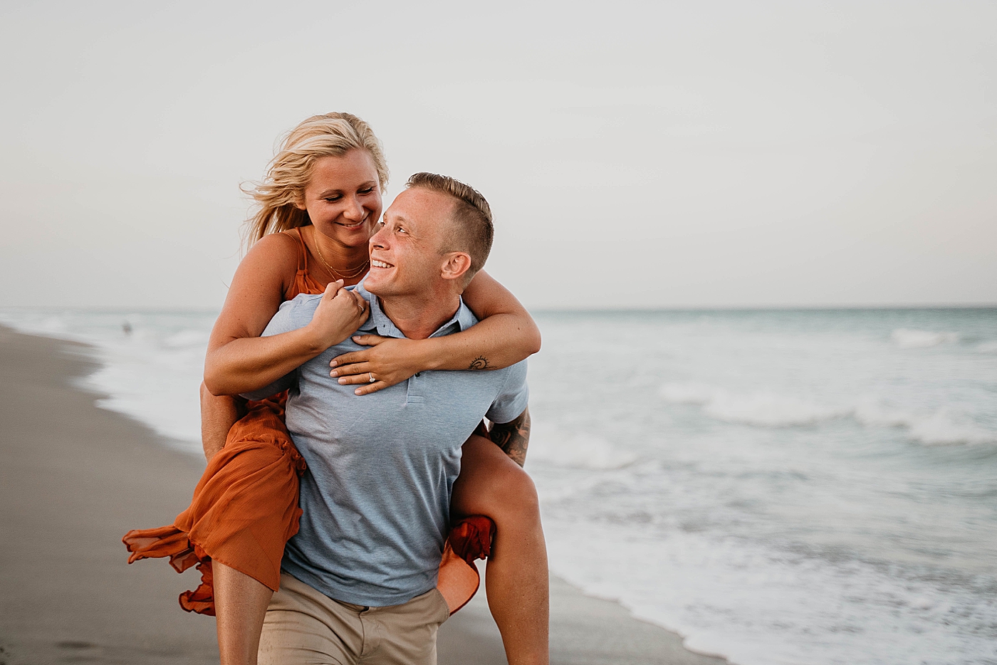 Couple piggy backing on the beach Jupiter Beach Engagement Photography captured by South Florida Engagement Photographer Krystal Capone Photography 