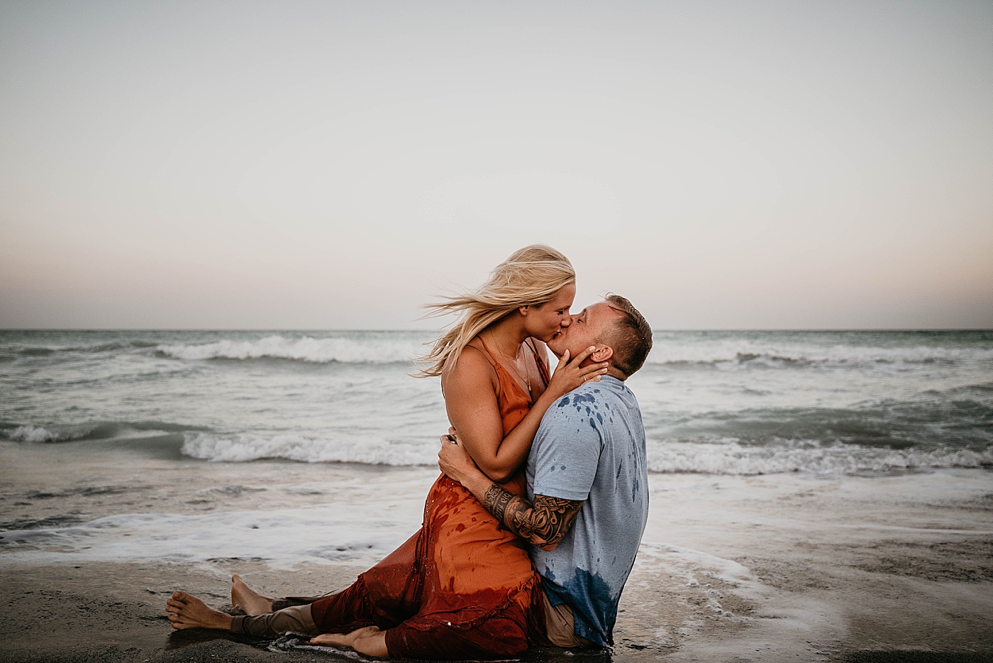 Couple sitting on the sand holding each other and kissing as waves come in Jupiter Beach Engagement Photography captured by South Florida Engagement Photographer Krystal Capone Photography 