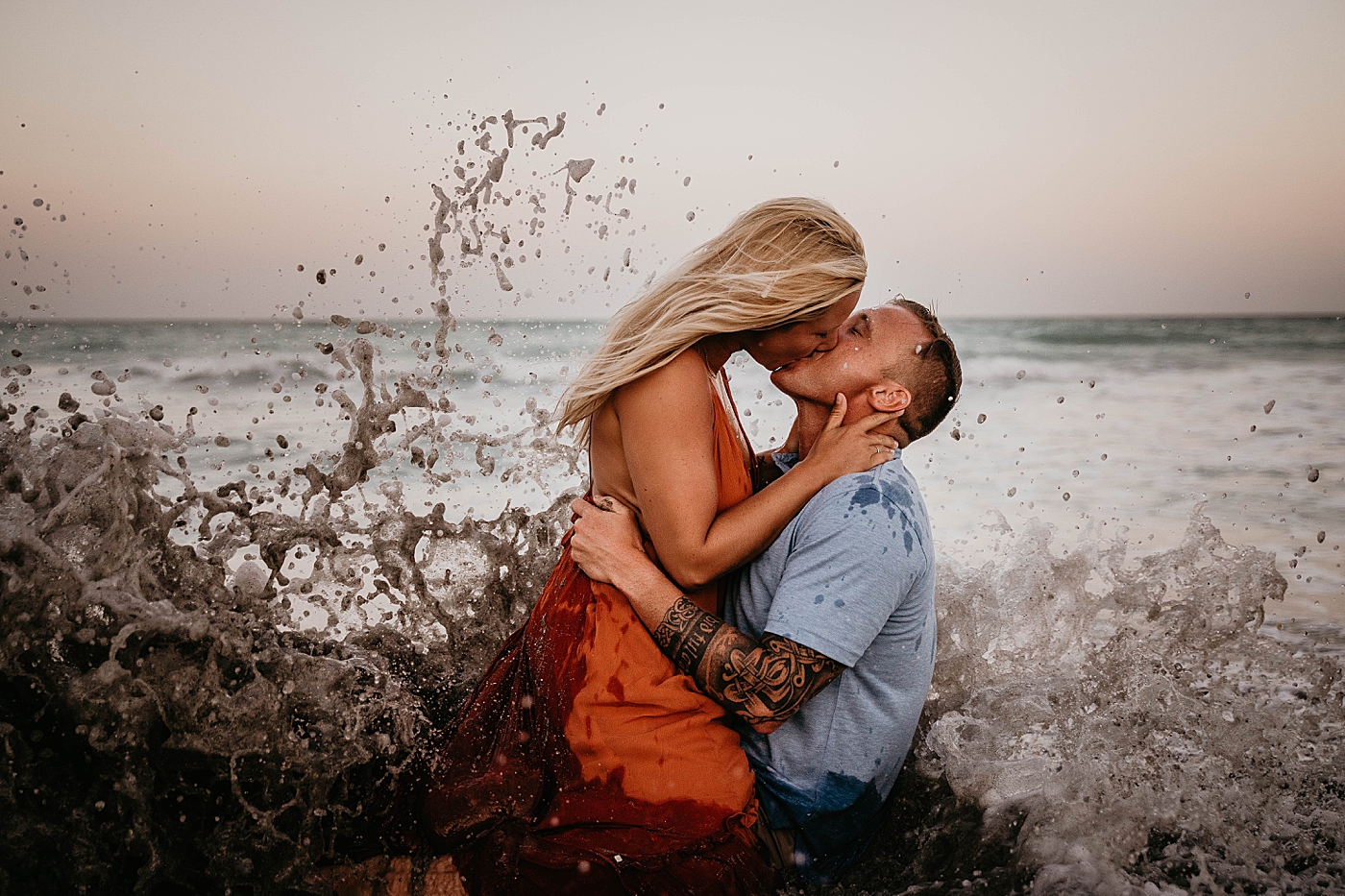 Couple kissing each other as wave crashes into them Jupiter Beach Engagement Photography captured by South Florida Engagement Photographer Krystal Capone Photography 