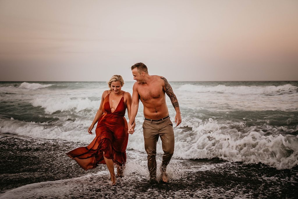 Couple holding hands and walking together by crashing waves Jupiter Beach Engagement Photography captured by South Florida Engagement Photographer Krystal Capone Photography 