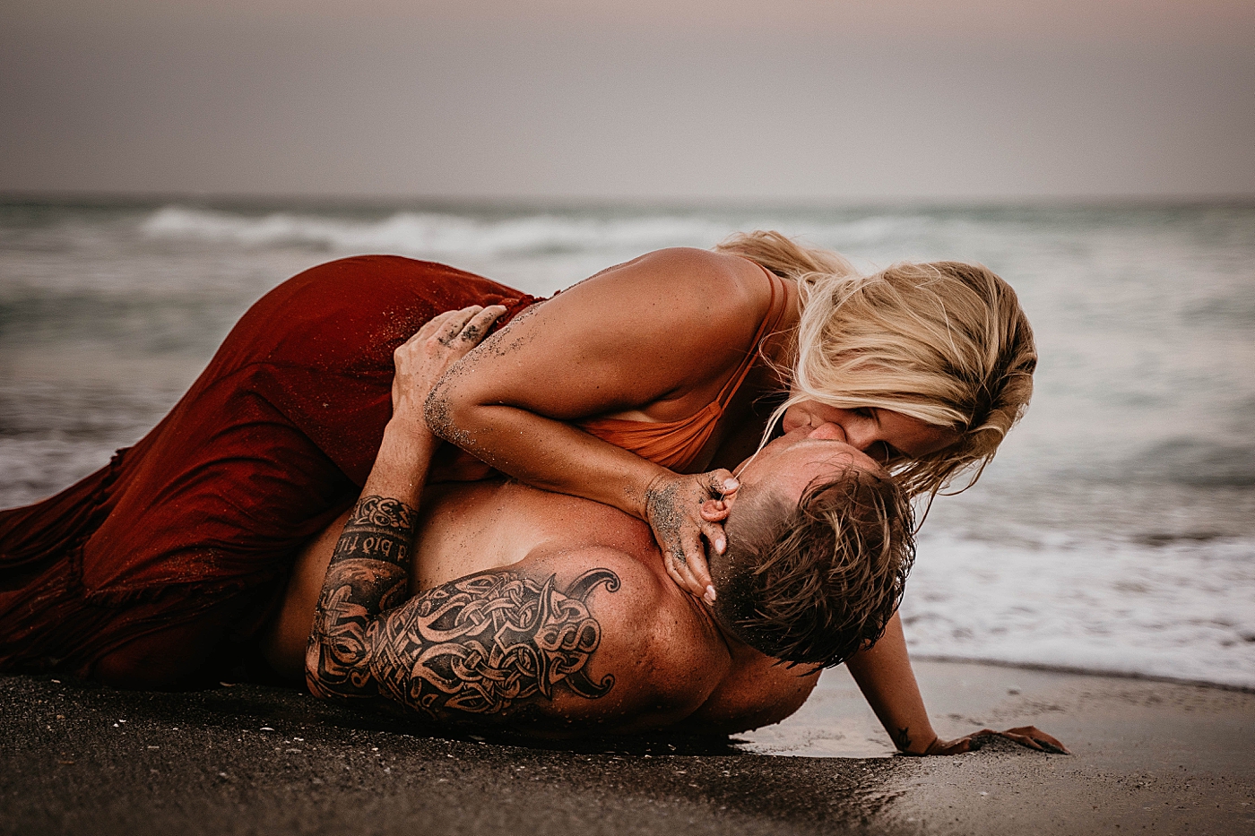 Man laying on sand with woman on top kissing on the beach Jupiter Beach Engagement Photography captured by South Florida Engagement Photographer Krystal Capone Photography 