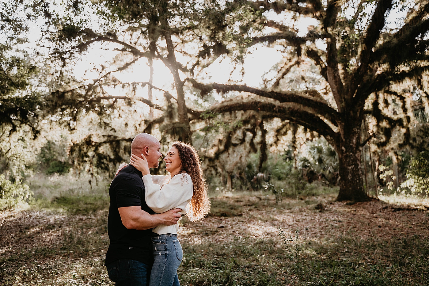 Couple hold each other in with the sun beaming in through trees Romantic Riverbend Park Engagement Photography captured by South Florida Photographer Krystal Capone Photography