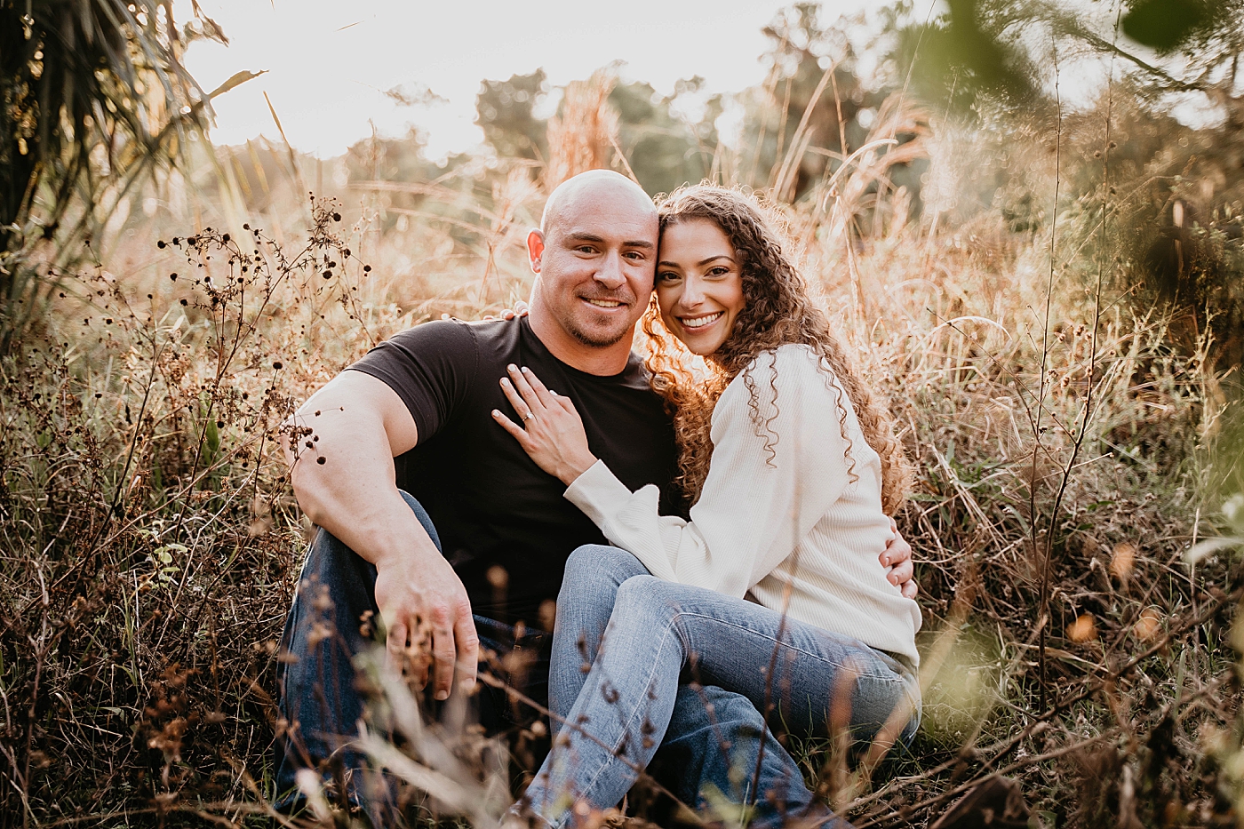 Couple sitting and holding each other on a tall grass field Romantic Riverbend Park Engagement Photography captured by South Florida Photographer Krystal Capone Photography