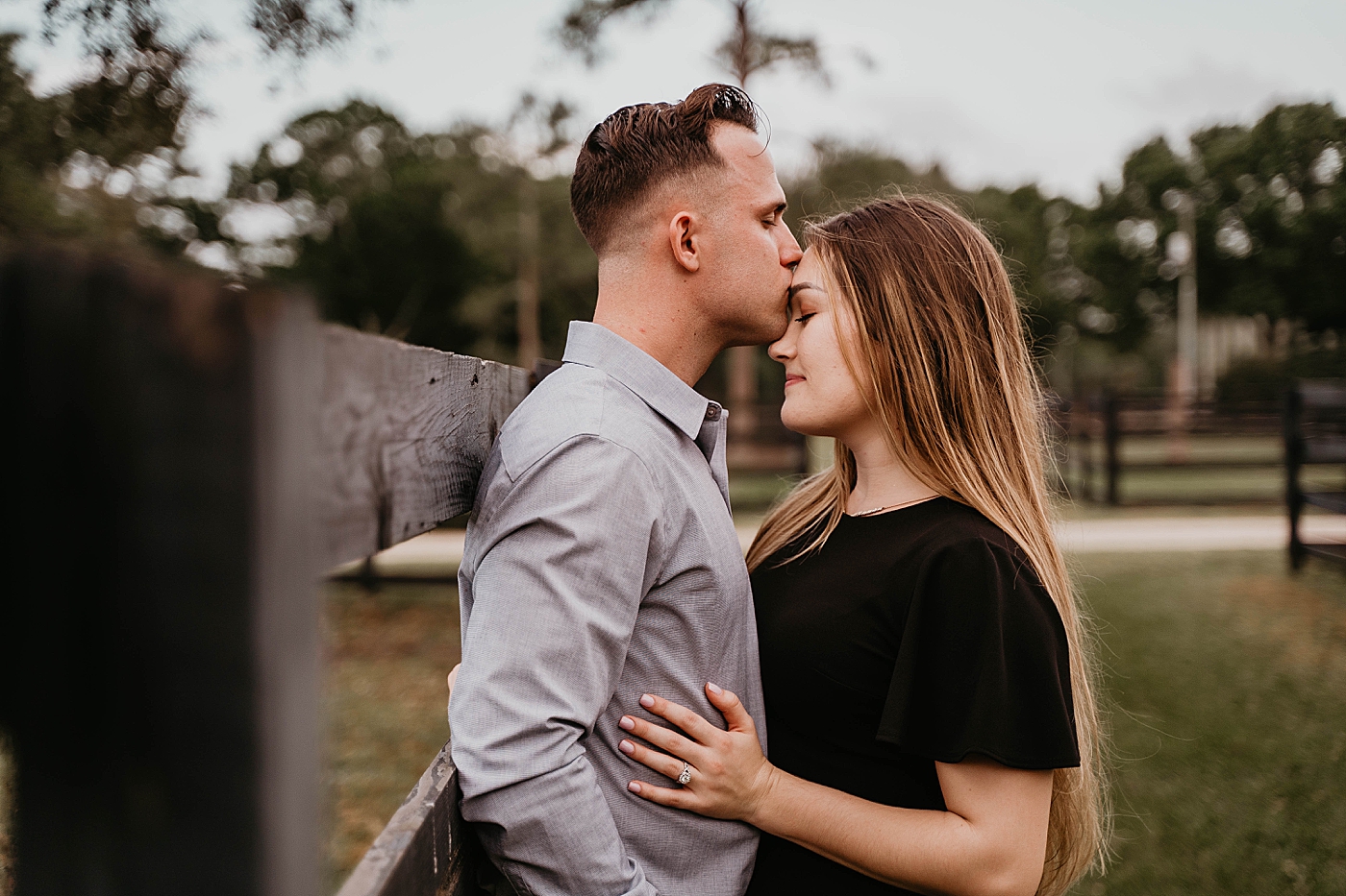 Couple leaning on farm fence with man kissing woman on forehead Rustic South Florida Engagement Photography captured by South Florida Engagement Photographer Krystal Capone Photography 