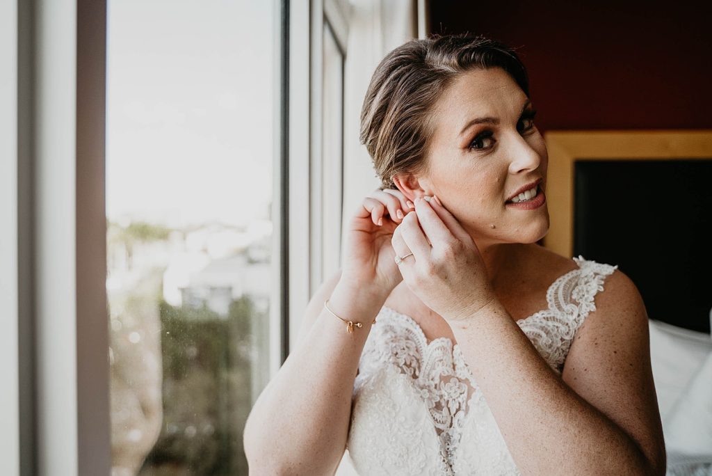 Bride Getting ready putting on earrings on by the window 94th Aero Squadron Miami Wedding Photography captured by South Florida Engagement Photographer Krystal Capone Photography 