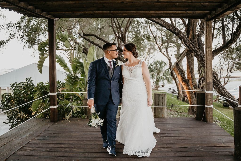Bride and Groom looking at each other and walking while Groom holds bouquet 94th Aero Squadron Miami Wedding Photography captured by South Florida Engagement Photographer Krystal Capone Photography 