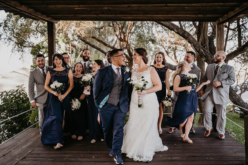 Bride and Groom walking together smiling and looking at each other with Bridal party behind them 94th Aero Squadron Miami Wedding Photography captured by South Florida Engagement Photographer Krystal Capone Photography 