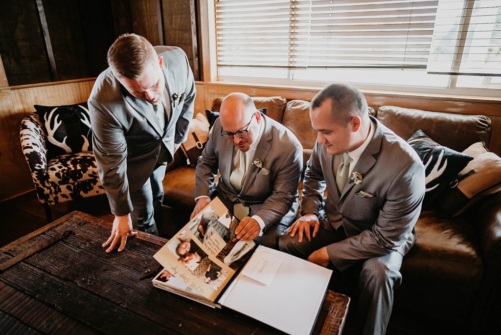 Groomsmen looking through picture book on the couch Ever After Farms Wedding Photography captured by South Florida Wedding Photographer Krystal Capone Photography 