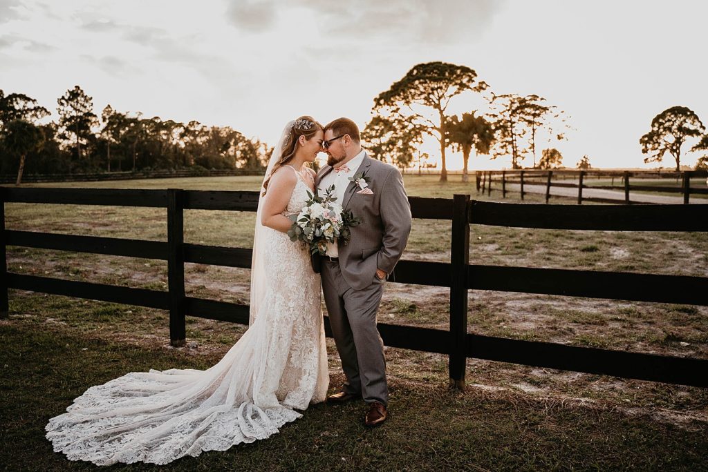 Bride and Groom resting their foreheads against each other next to fence with the sun setting Ever After Farms Wedding Photography captured by South Florida Wedding Photographer Krystal Capone Photography 