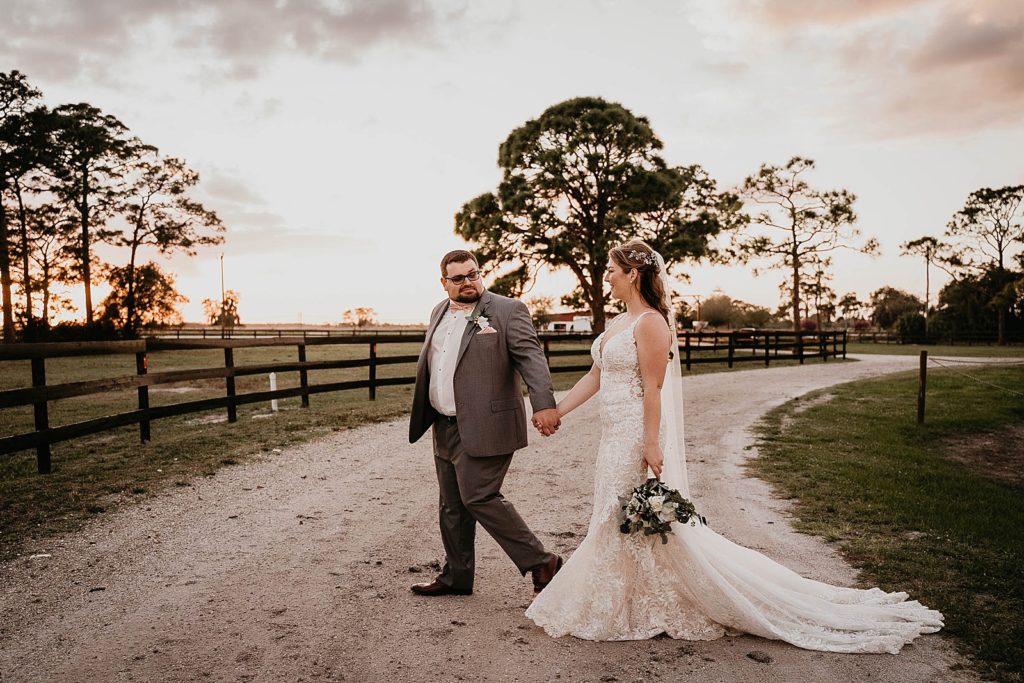 Groom holding Bride's hand and leading her across dirt path Ever After Farms Wedding Photography captured by South Florida Wedding Photographer Krystal Capone Photography 