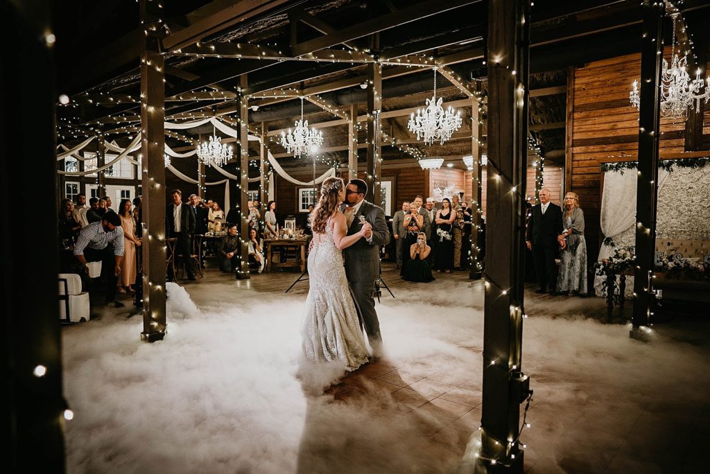 Bride and Groom kissing during First dance with all the guests watching with lights from chandeliers and strings lights everywhere Ever After Farms Wedding Photography captured by South Florida Wedding Photographer Krystal Capone Photography 