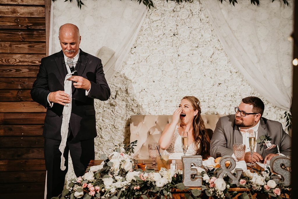 Father giving fun toast speech with Bride laughing sitting at sweetheart table Ever After Farms Wedding Photography captured by South Florida Wedding Photographer Krystal Capone Photography 