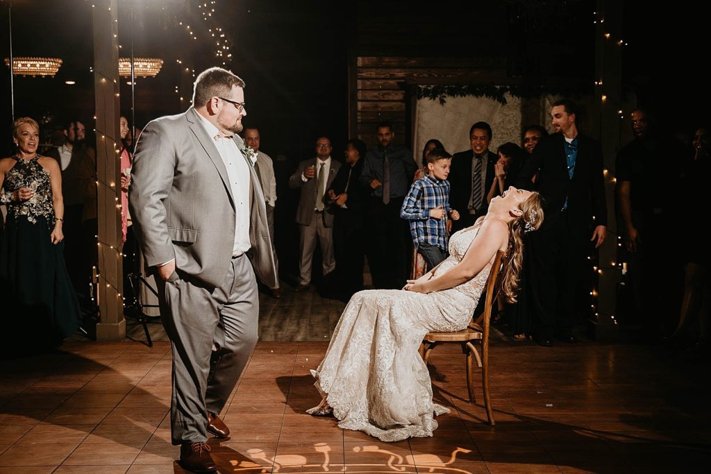 Groom doing goofy seductive dance for garter toss Reception Bride laughing sitting down Ever After Farms Wedding Photography captured by South Florida Wedding Photographer Krystal Capone Photography 