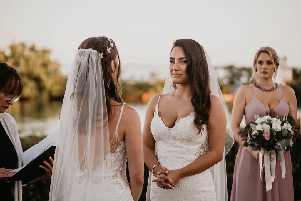 Brides looking at each other during Homily ceremony with maid of honor holding bouquet in hand Hawks Cay Resort Wedding Photography captured by South Florida Wedding Photographer Krystal Capone Photography