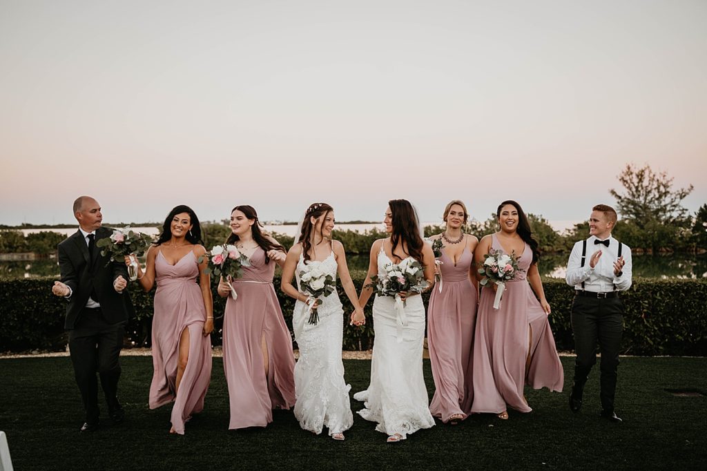 Brides holding hands walking together with Bridal party following behind them Hawks Cay Resort Wedding Photography captured by South Florida Wedding Photographer Krystal Capone Photography