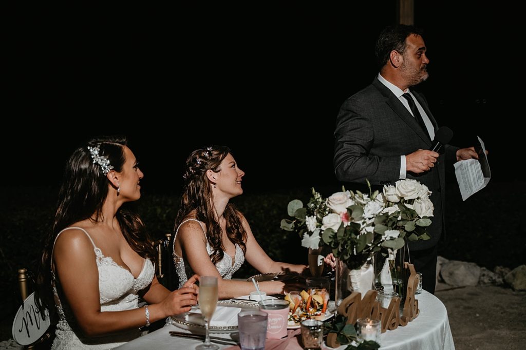 Brides at sweetheart table listening to speech Hawks Cay Resort Wedding Photography captured by South Florida Wedding Photographer Krystal Capone Photography