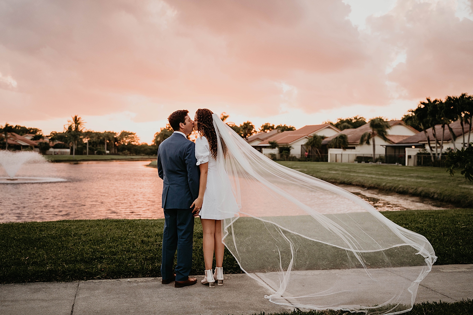 Bride and Groom holding hands and kissing in front of lake with water fountain Intimate South Florida Wedding Photography captured by South Florida Wedding Photographer Krystal Capone Photography 