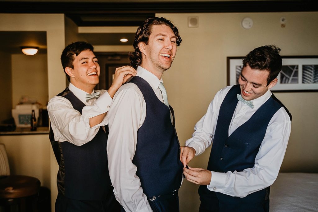 Groom getting help putting on vests by groomsmen getting ready Jupiter Beach Resort Wedding Photography captured by South Florida Wedding Photographer Krystal Capone Photography 
