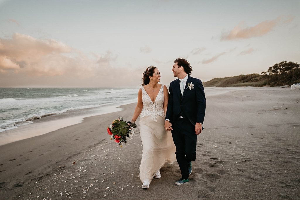 Bride and Groom strolling on the sand with sneakers on with seashells on the ground Jupiter Beach Resort Wedding Photography captured by South Florida Wedding Photographer Krystal Capone Photography 