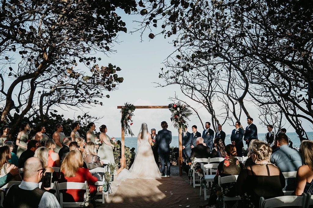 wide shot of tropical beach ceremony with Bride and Groom listing to Homily Jupiter Beach Resort Wedding Photography captured by South Florida Wedding Photographer Krystal Capone Photography 