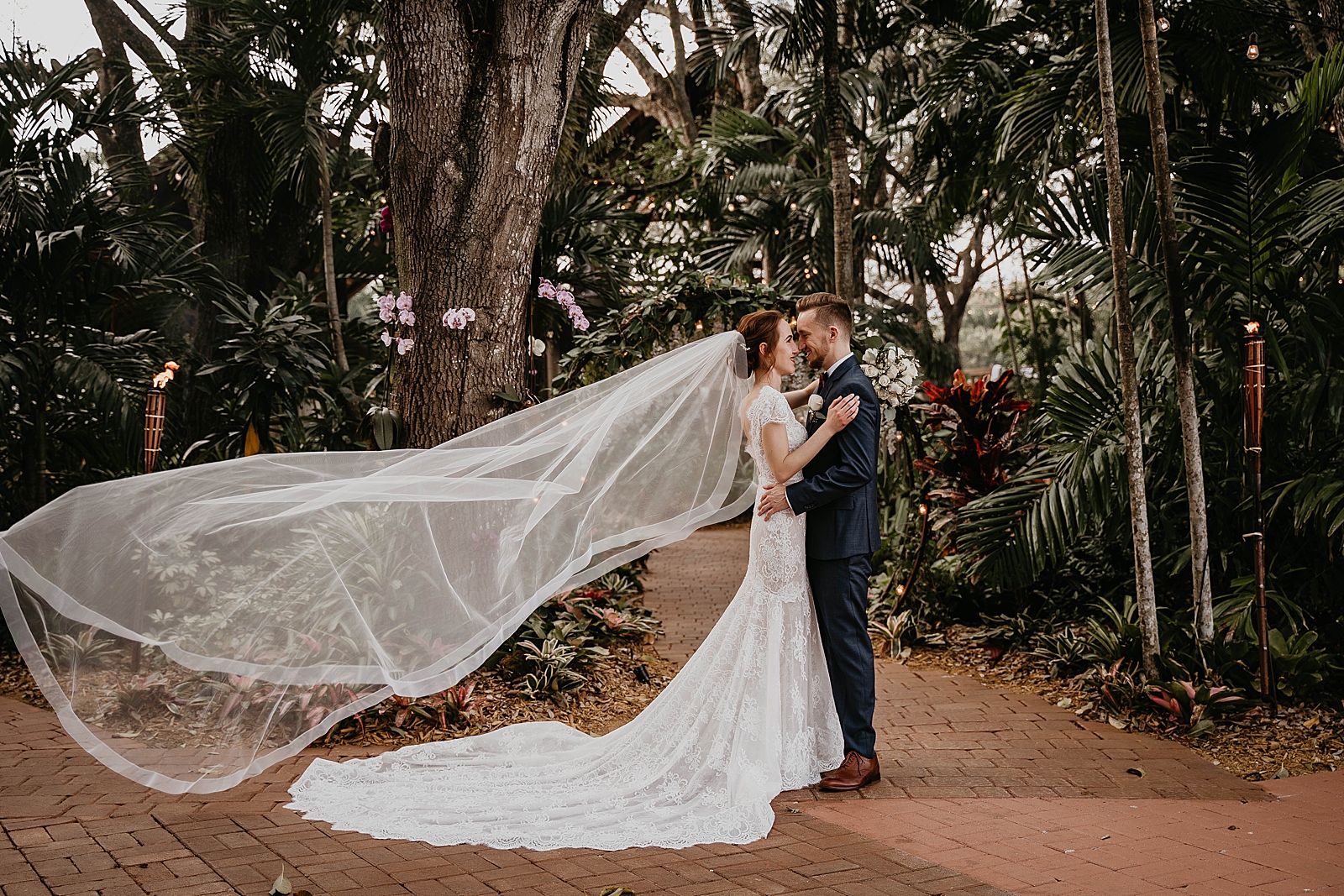 Bride and Groom holding each other close with flowing long veil in botanical garden area Living Sculptures Sanctuary Wedding Photography captured by South Florida Wedding Photographer Krystal Capone Photography 