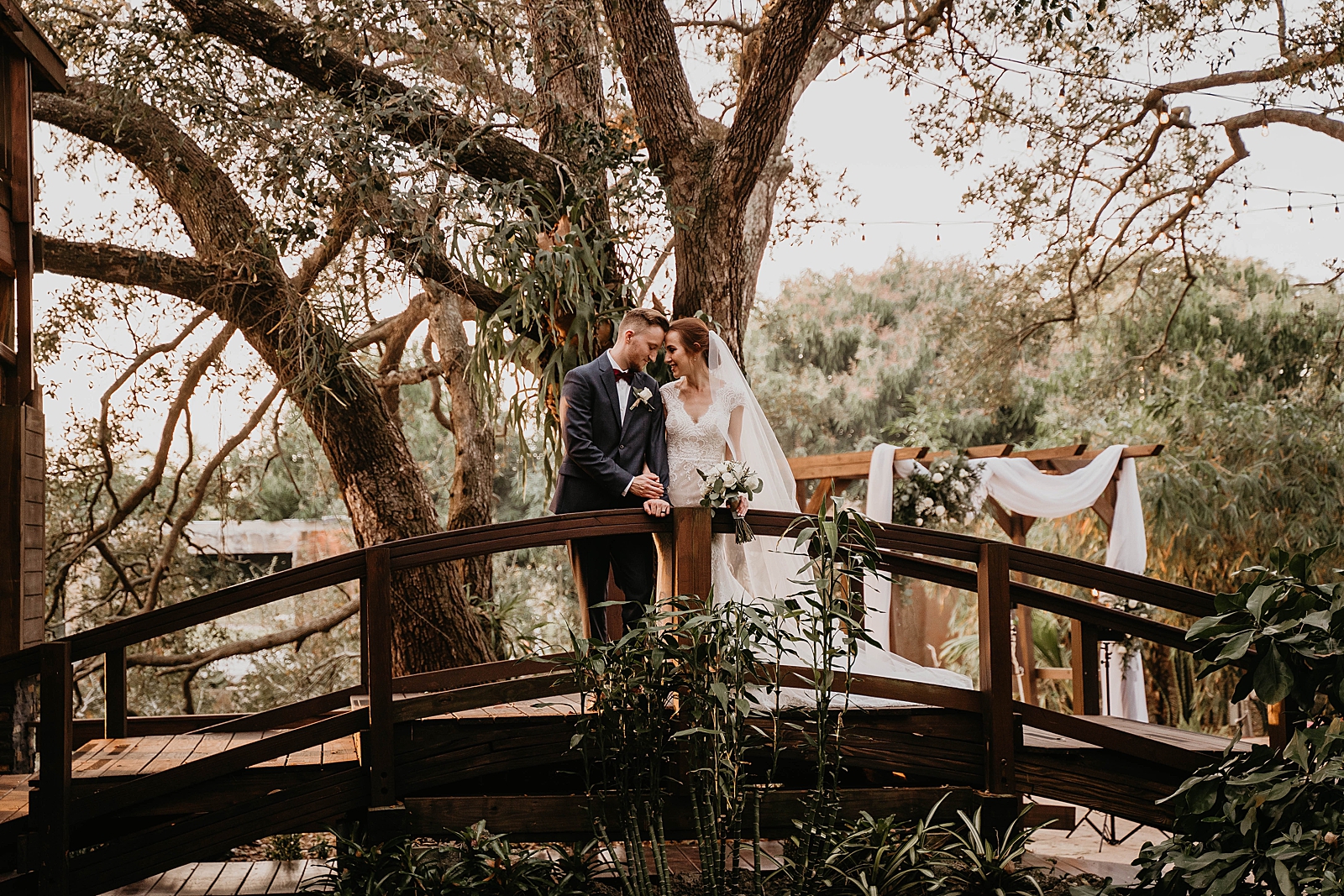Bride and Groom touching their foreheads on arch bridge with lots of greenery Living Sculptures Sanctuary Wedding Photography captured by South Florida Wedding Photographer Krystal Capone Photography 
