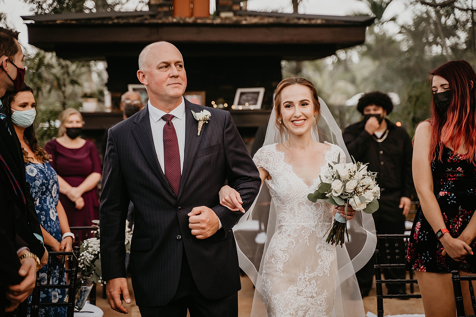 Bride and father arm in arm entering Ceremony with mask on attendees Living Sculptures Sanctuary Wedding Photography captured by South Florida Wedding Photographer Krystal Capone Photography 