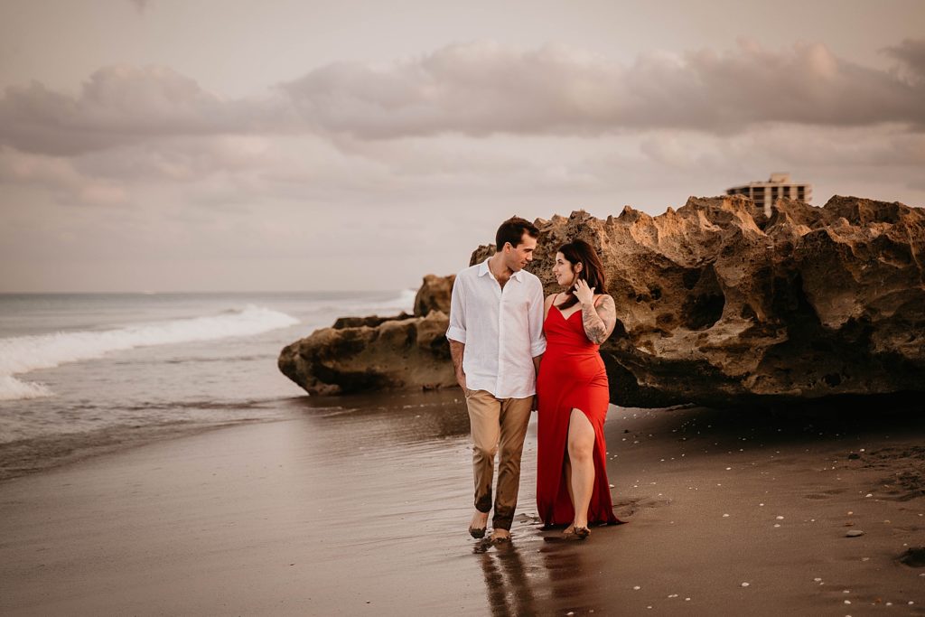 Couple holding hands walking barefoot on the wet sand looking at each other Palm Beach Engagement Photography captured by South Florida Engagement Photographer Krystal Capone Photography 