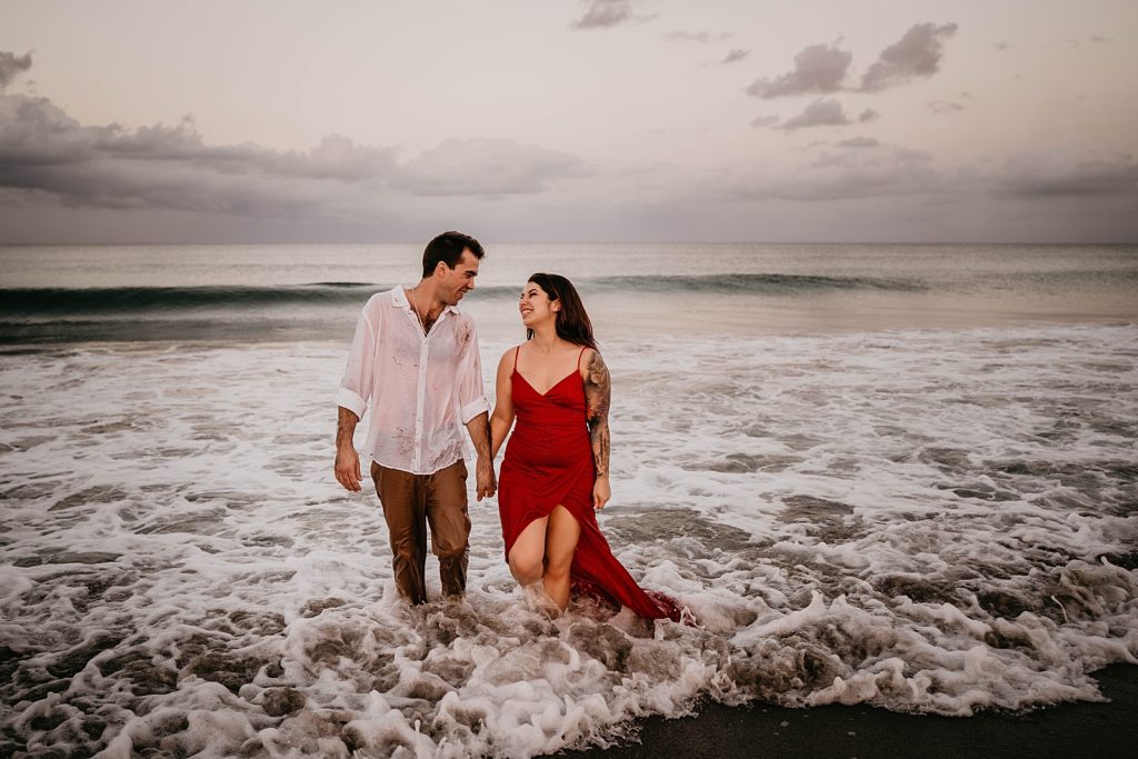 Couple walking in shallow ocean water on the beach looking at each other Palm Beach Engagement Photography captured by South Florida Engagement Photographer Krystal Capone Photography 