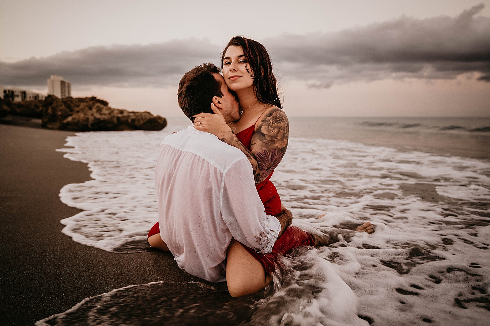 Lady saddles man on the beach with ocean water coming in Palm Beach Engagement Photography captured by South Florida Engagement Photographer Krystal Capone Photography 