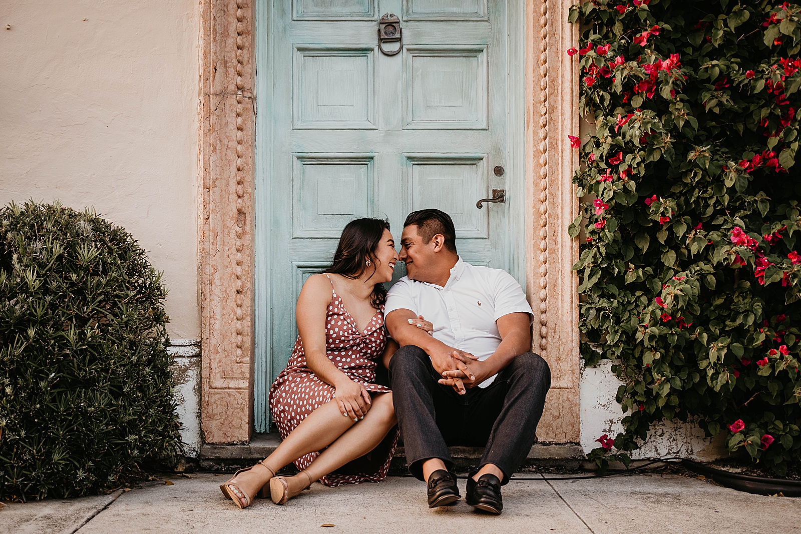 Couple sitting down together in front of light blue door and nuzzle their noses Palm Beach Island Engagement Photography captured by South Florida Engagement Photographer Krystal Capone Photography 