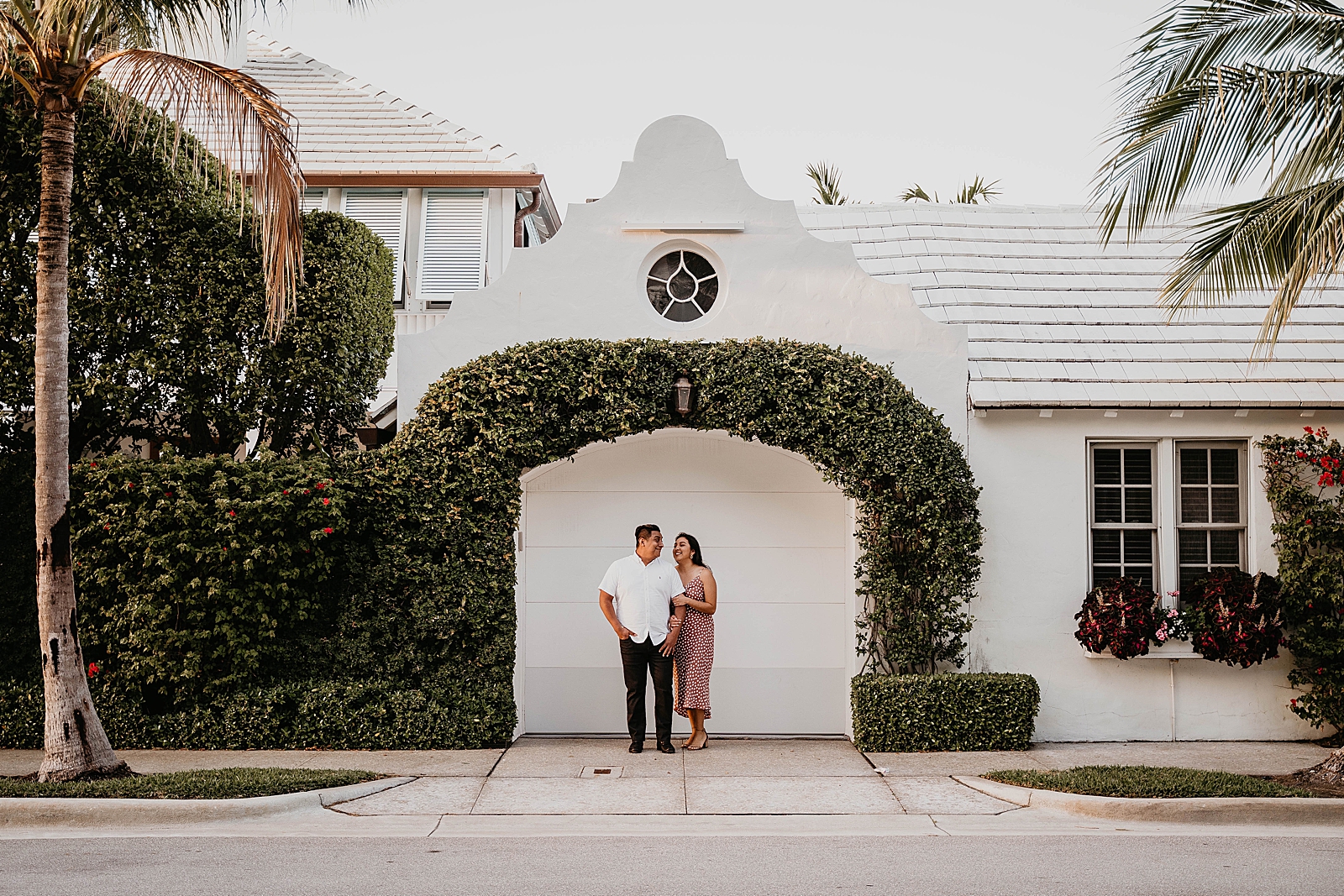 Couple standing under a green hedge archway in front of a house Palm Beach Island Engagement Photography captured by South Florida Engagement Photographer Krystal Capone Photography 