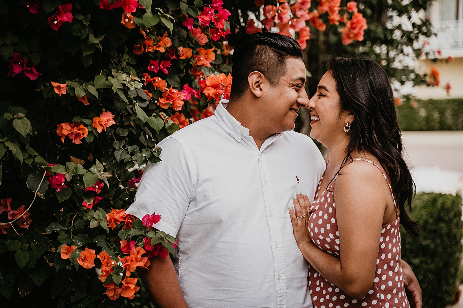 Couple touching their noses in front of greenery with bright red flowers Palm Beach Island Engagement Photography captured by South Florida Engagement Photographer Krystal Capone Photography 
