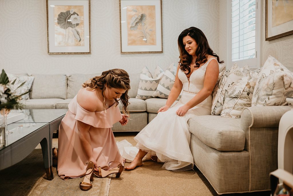 Bride getting help from Bridesmaid putting on wedding heels Pelican Club Wedding Photography captured by South Florida Wedding Photographer Krystal Capone Photography 