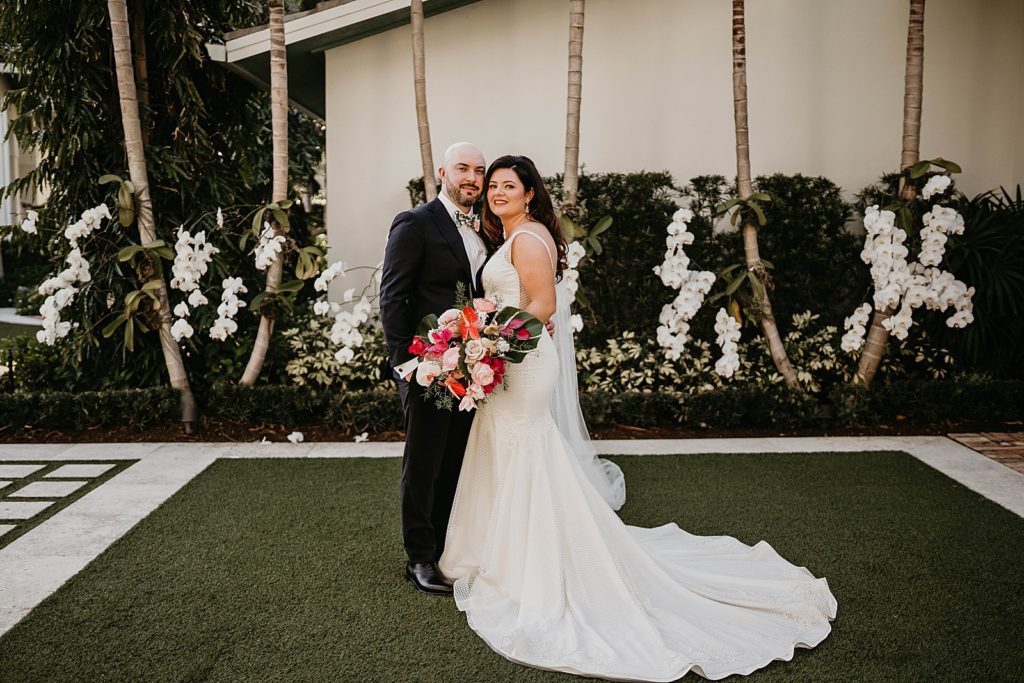 Bride and Groom posing together with tropical bright red bouquet Pelican Club Wedding Photography captured by South Florida Wedding Photographer Krystal Capone Photography 