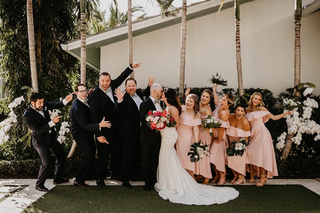 Bride and Groom kissing with Groomsmen and Bridesmaids celebrating and reacting Pelican Club Wedding Photography captured by South Florida Wedding Photographer Krystal Capone Photography 