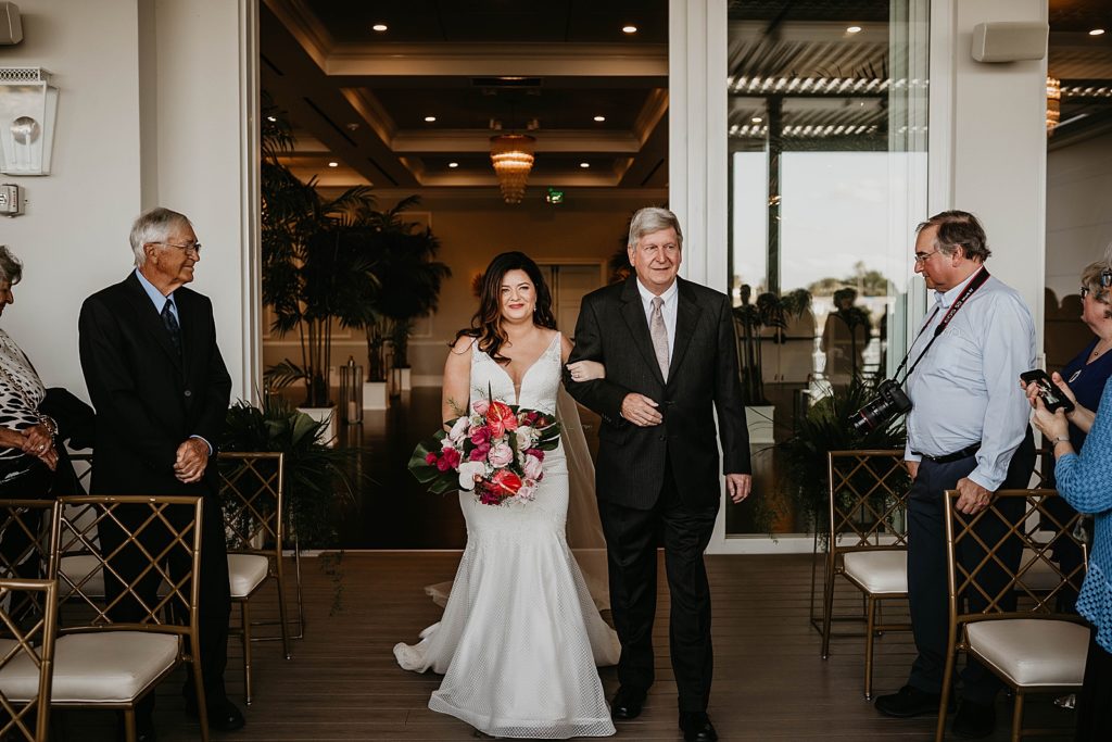 Bride and father entering ceremony arm in arm with red bouquet Pelican Club Wedding Photography captured by South Florida Wedding Photographer Krystal Capone Photography 