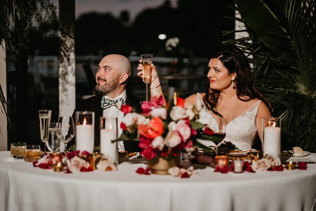 Bride and Groom raising glasses up for toast at sweetheart table Pelican Club Wedding Photography captured by South Florida Wedding Photographer Krystal Capone Photography 
