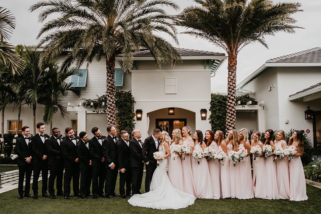 Bride and Groom kissing with whole Bridal party Pelican Club Wedding Photography captured by South Florida Wedding Photographer Krystal Capone Photography