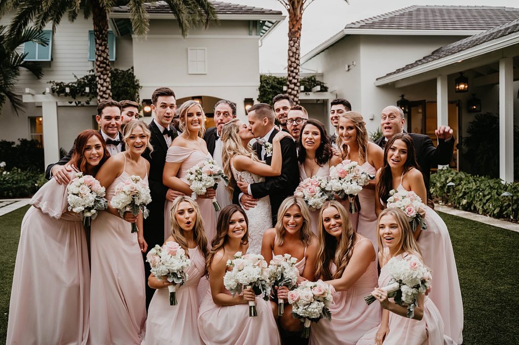 Bride and Groom kissing with Bridal party surrounding them Pelican Club Wedding Photography captured by South Florida Wedding Photographer Krystal Capone Photography